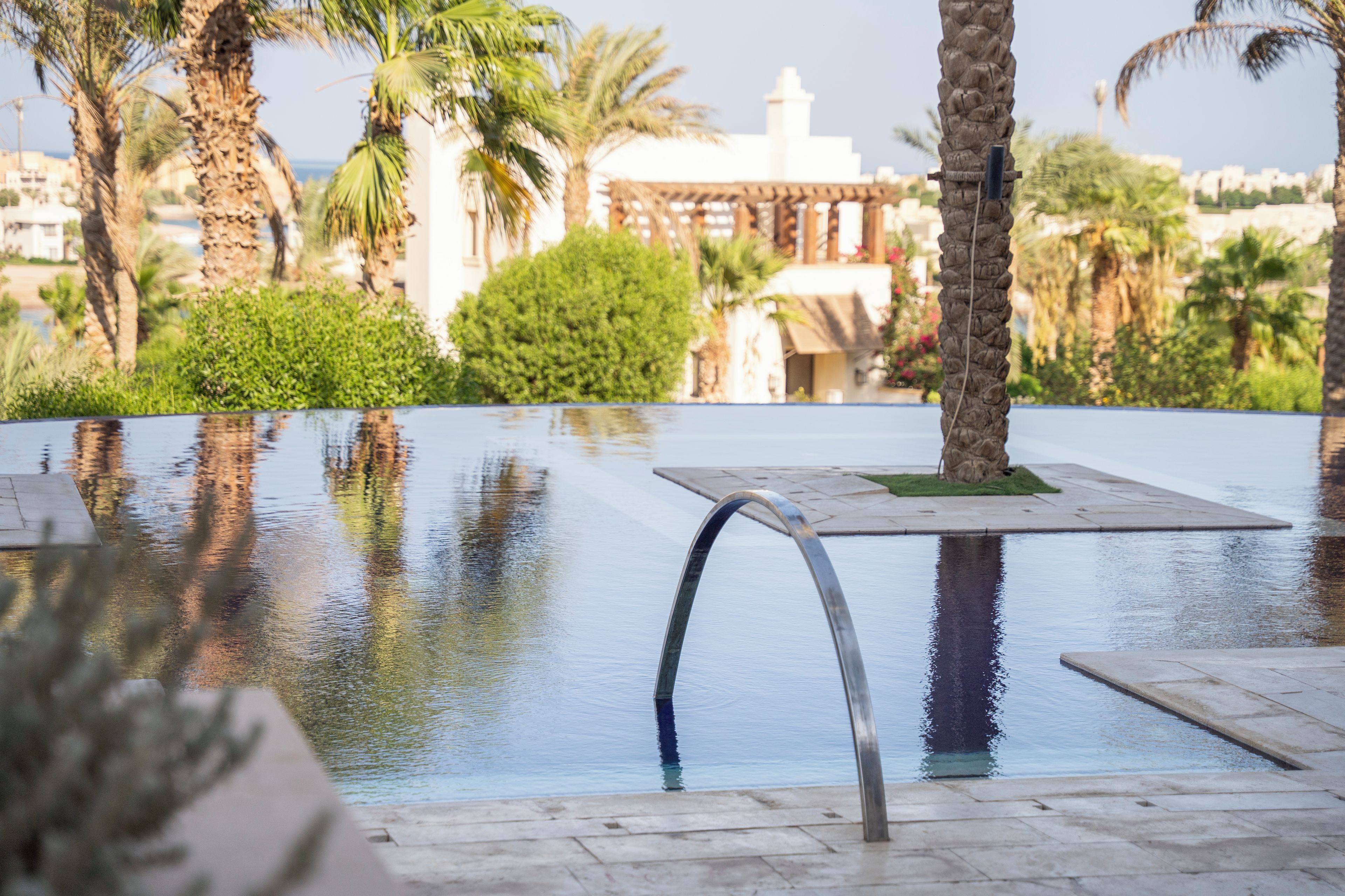 Ein Pool mit geschwungener Kante, umgeben von Palmen und einem Gebäude im Hintergrund.