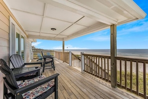 Eine Holzterrasse mit Sitzgelegenheiten und Blick auf den Strand.
