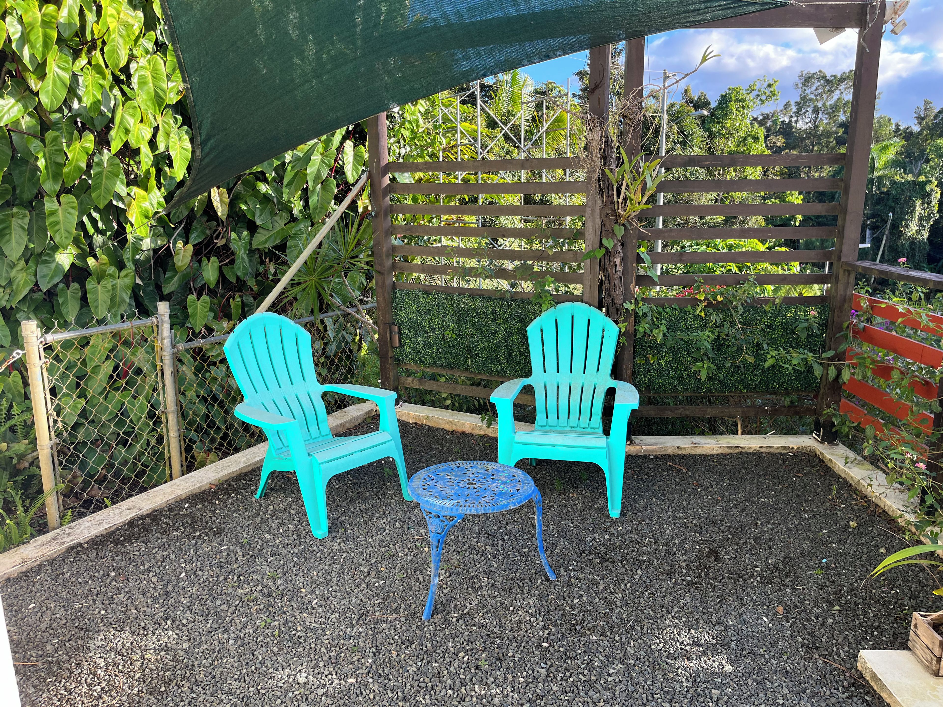 Un espace patio avec deux fauteuils Adirondack turquoise et une petite table bleue, entouré de gravier et d’une clôture en bois.