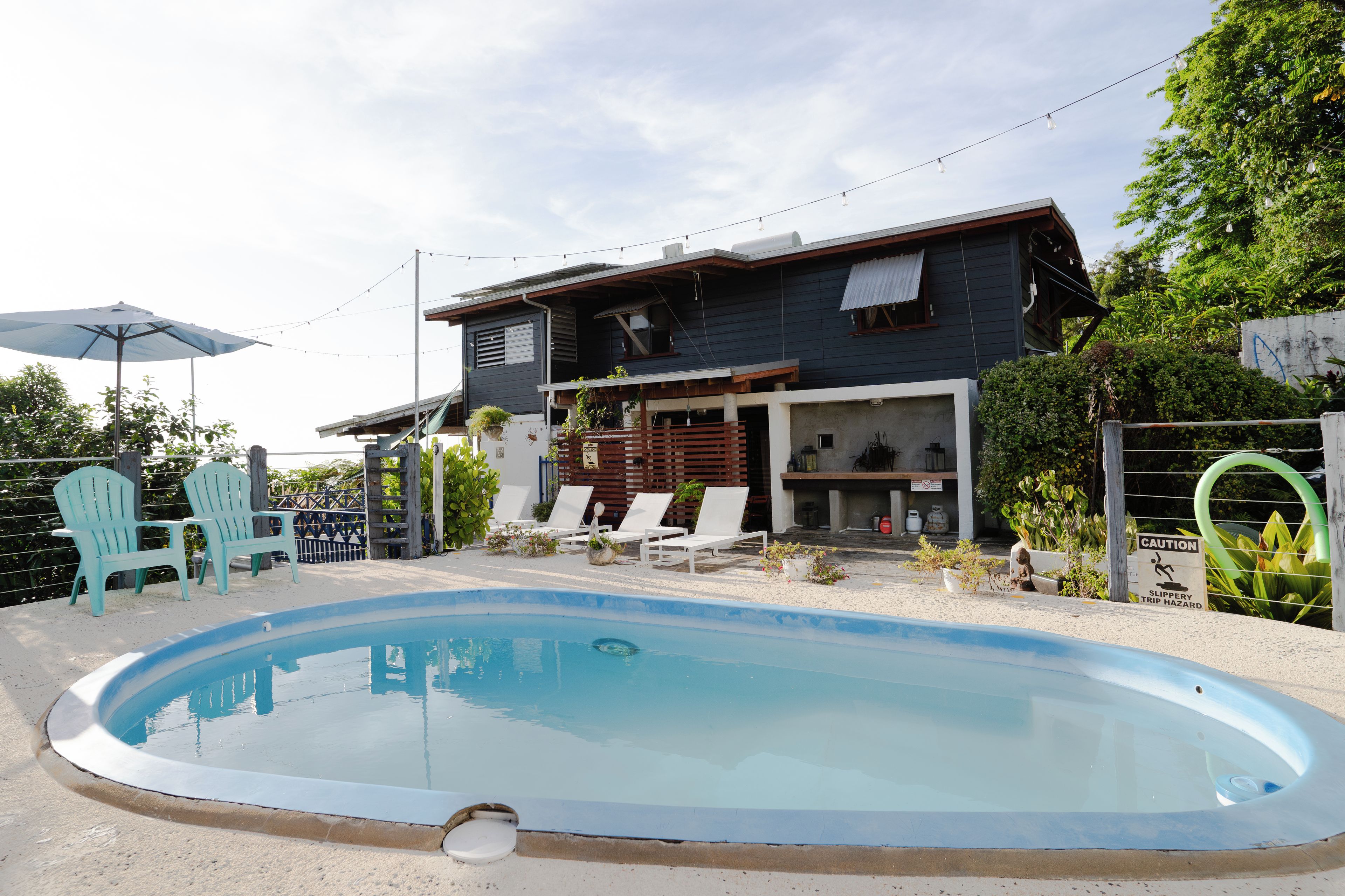 A residential property with a swimming pool, outdoor seating, and a house with a dark facade.