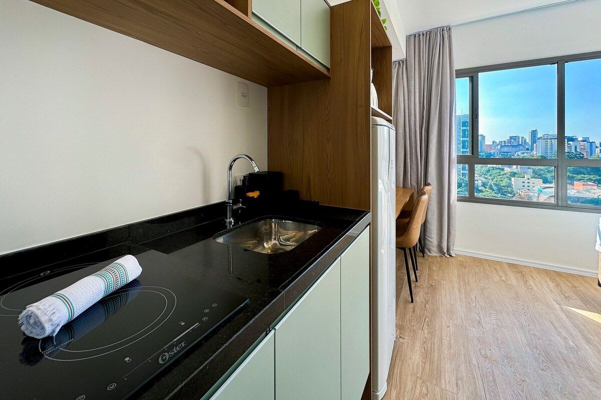 A modern kitchen with a black countertop, a built-in oven, and a view of a cityscape through large windows.