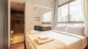 Et hotelværelse med seng, skrivebord, stol, bruseområde og udsigt over byen gennem vinduet.