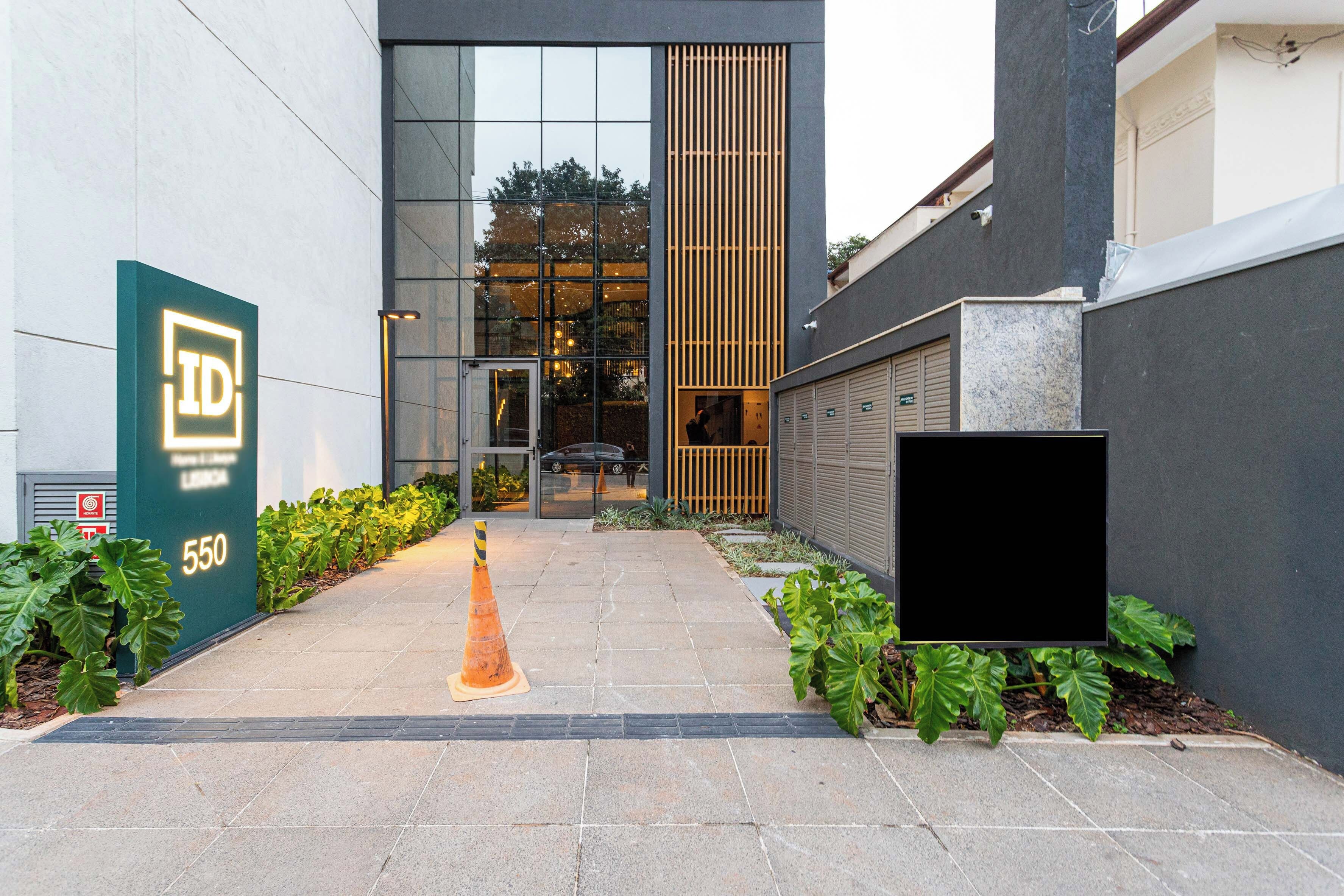 A modern building entrance with a glass facade, a green sign with 'ID' and the number '550', and a paved pathway leading to the entrance.