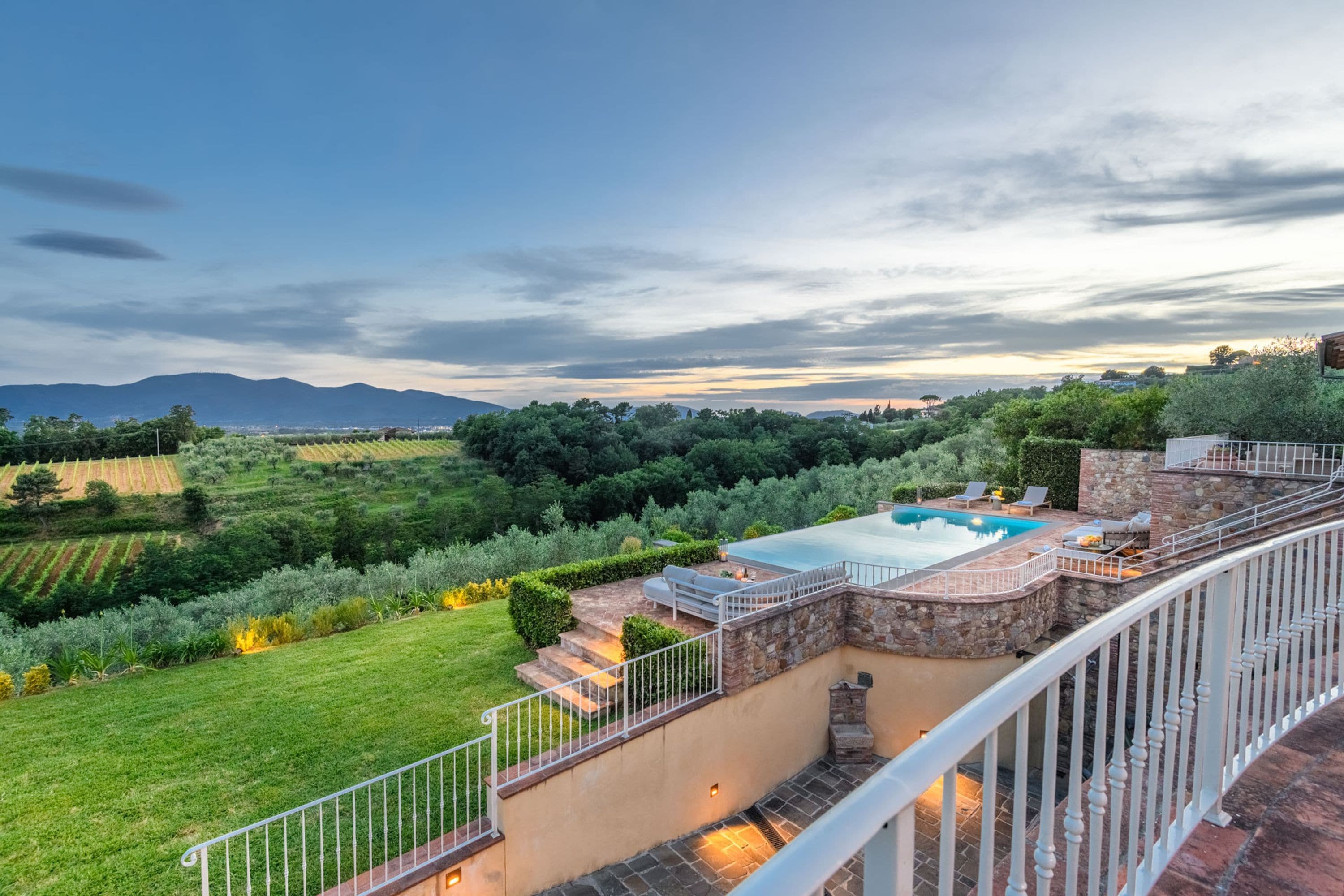 A pool area with a stone wall and steps leading down to a grassy lawn.