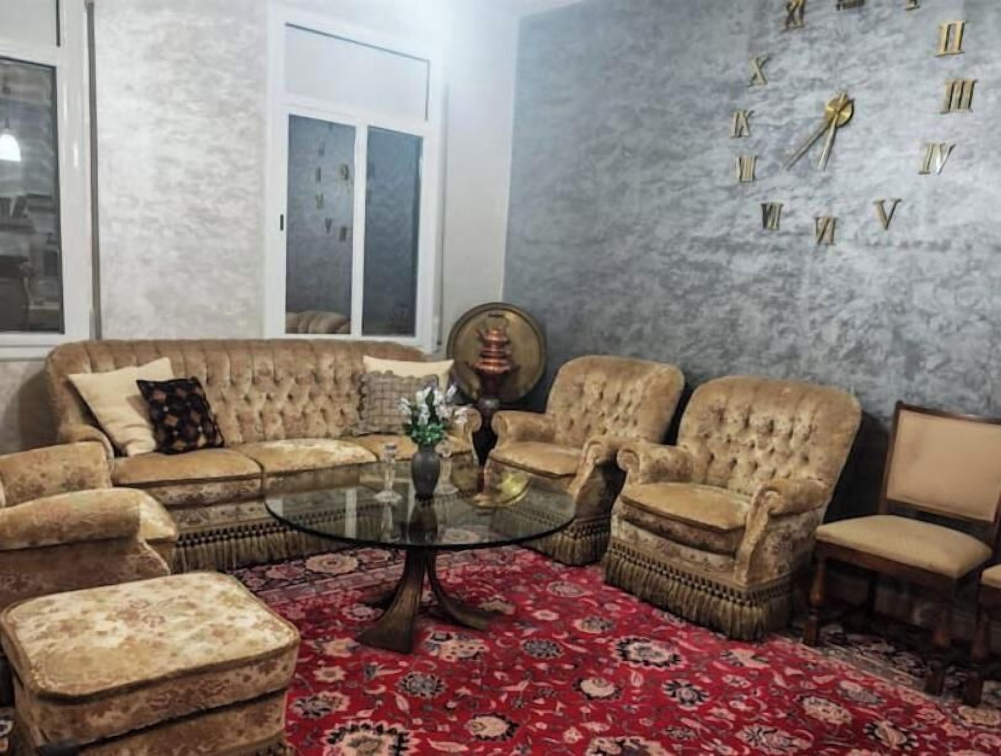 Ein Wohnzimmer mit einer Sofagarnitur, Sesseln, einem Couchtisch und einer Wanduhr.