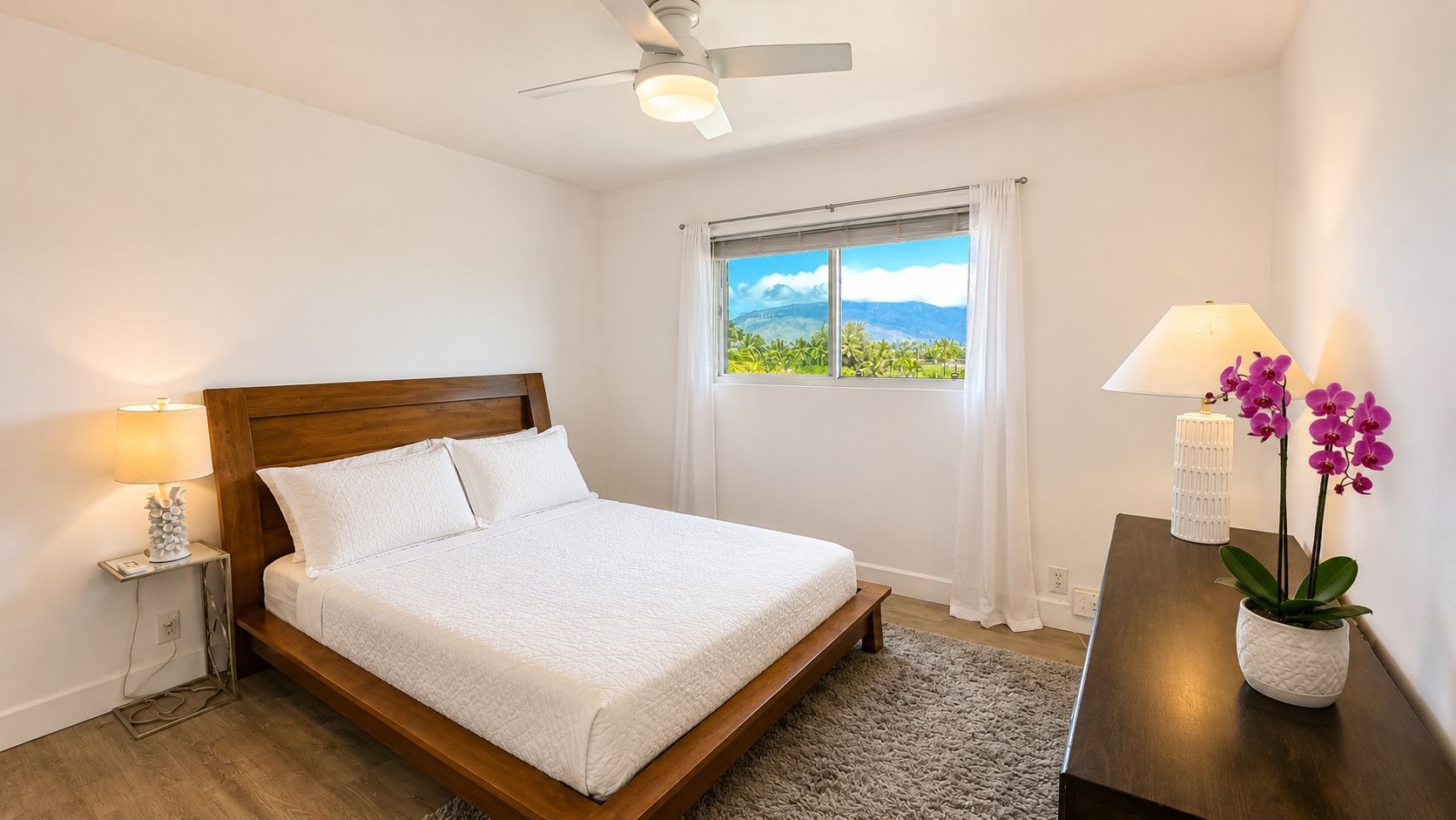 Une chambre à coucher comprenant un lit, une table de chevet, une lampe, une fenêtre avec vue et un ventilateur de plafond.
