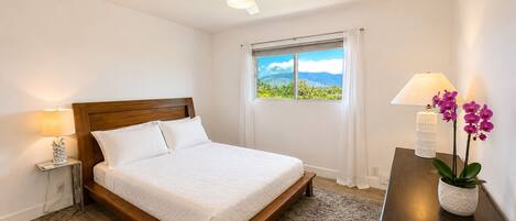 Une chambre à coucher comprenant un lit, une table de chevet, une lampe, une fenêtre avec vue et un ventilateur de plafond.