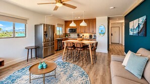 A modern kitchen with a dining area, wooden cabinets, and a view of the outdoors. - Where Paradise Meets the Waves Remodeled Kihei Condo with Ocean Views (Kihei)