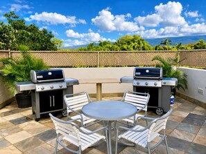 Eine Terrasse im Freien mit zwei Weber-Grills, einem runden Tisch und vier Stühlen.