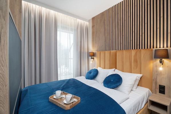 A hotel room with a bed, curtains, a wooden headboard, a nightstand, and a tray with cups. - Szklarska Poreba | Górna 19A | Air-conditioned Studio | Swimming Pool and Gym (Szklarska Poręba)