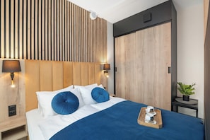 A modern hotel room with a large bed, a wooden slatted headboard, two bedside lamps, a nightstand, a small table with a tray of cups, and a potted plant. - Szklarska Poreba | Górna 19A | Air-conditioned Studio | Swimming Pool and Gym (Szklarska Poręba)