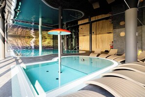 A modern indoor swimming pool with a waterfall feature, lounge chairs, and a wooden wall. - Szklarska Poreba | Górna 19A | Air-conditioned Studio | Swimming Pool and Gym (Szklarska Poręba)