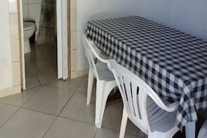 A small room with a checkered table and two white plastic chairs. A toilet is visible in the background. - Pousada do Osvaldo Imbé (Imbé)