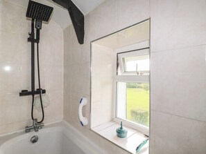 Ein Badezimmer mit einer Badewanne, einer Dusche und einem Fenster mit Blick auf eine grüne Landschaft.
