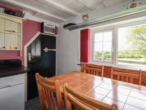 Eine Küche mit Esstisch, Stühlen, einem schwarzen Kühlschrank, einem weißen Schrank und einem Fenster mit Blick auf Grünflächen.