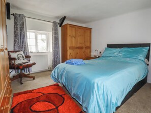 Ein Schlafzimmer mit einem Bett, einem Holzschrank, einem Stuhl, einem Heizkörper und einem Fenster mit Vorhängen.