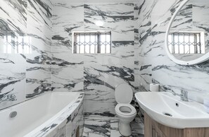 A bathroom with a marble floor, a bathtub, a toilet, and a sink. - Nice 4-bedroom house in Bulawayo perfect for your getaway (Bulawayo)
