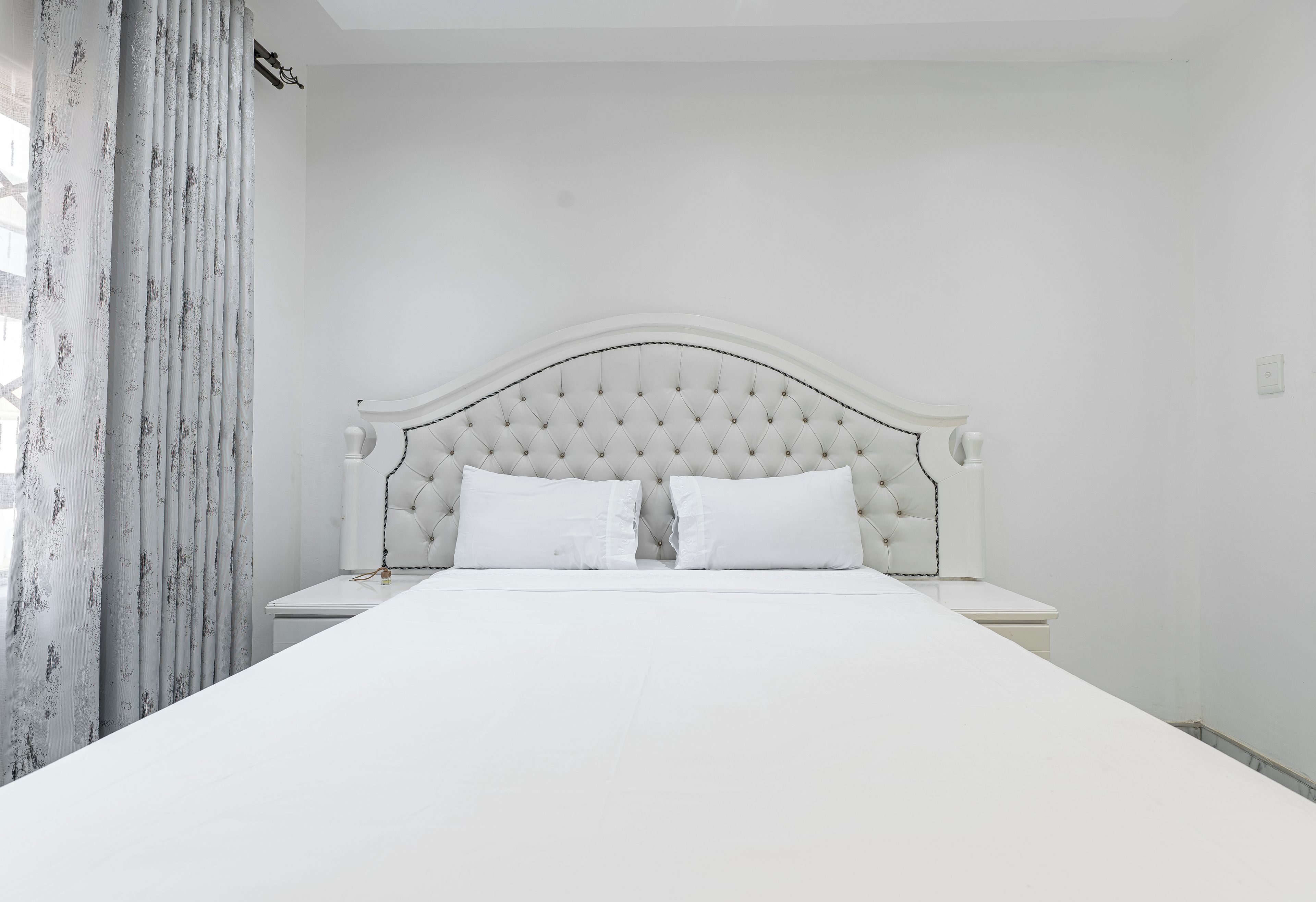 A bed with a tufted headboard, two pillows, and a white nightstand.