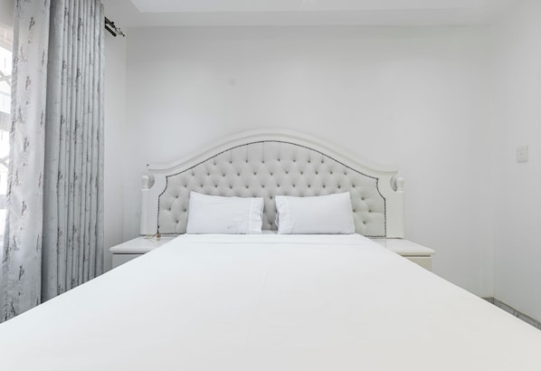 A bed with a tufted headboard, two pillows, and a white nightstand.