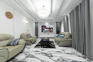 A modern living room with two sofas, a coffee table, a TV, and a chandelier. - Nice 4-bedroom house in Bulawayo perfect for your getaway (Bulawayo)