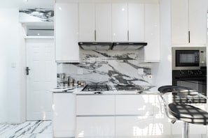 A modern kitchen with white cabinetry, a black and white marble backsplash, a built-in microwave, and a gas stove.