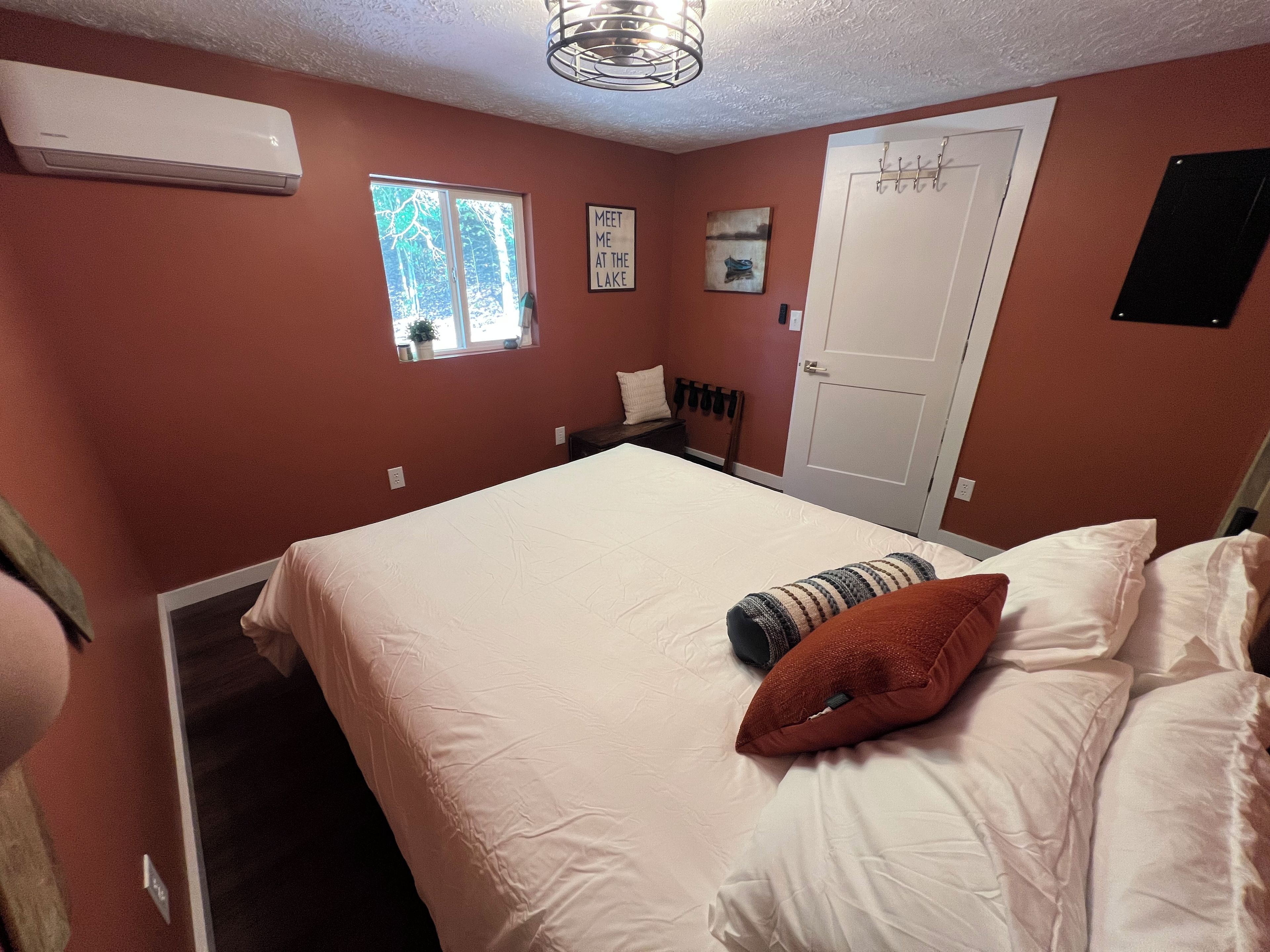 Un dormitorio con una cama, una ventana, una puerta y un aire acondicionado de pared.