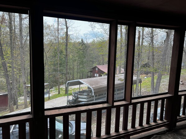 A view from a window with a wooden railing, overlooking a cabin and a covered vehicle in a forested area.