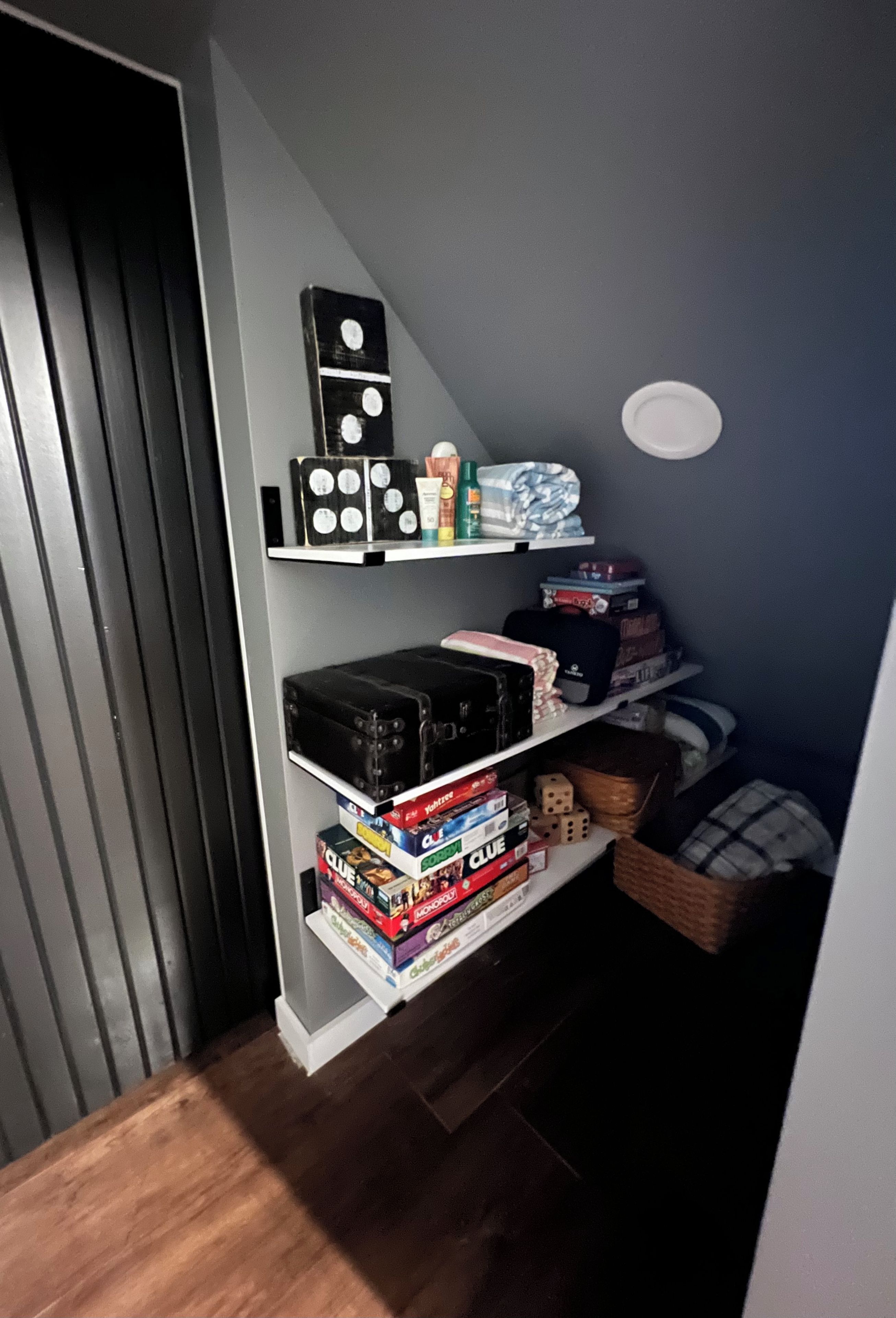 Un espace de rangement doté d’étagères contenant divers objets, notamment des jeux de société, une valise noire et un petit objet blanc.