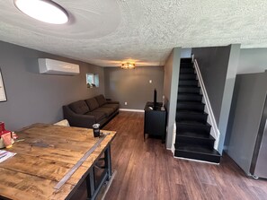 A modern living space with a wooden dining table, a sofa, a staircase, and a ceiling light fixture.