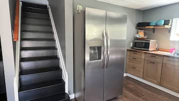 A kitchen with a stainless steel refrigerator, wooden cabinets, a microwave, and a wooden staircase.