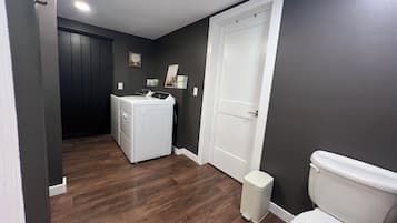 Une buanderie équipée d’un lave-linge et d’un sèche-linge, de toilettes blanches et d’une poubelle.