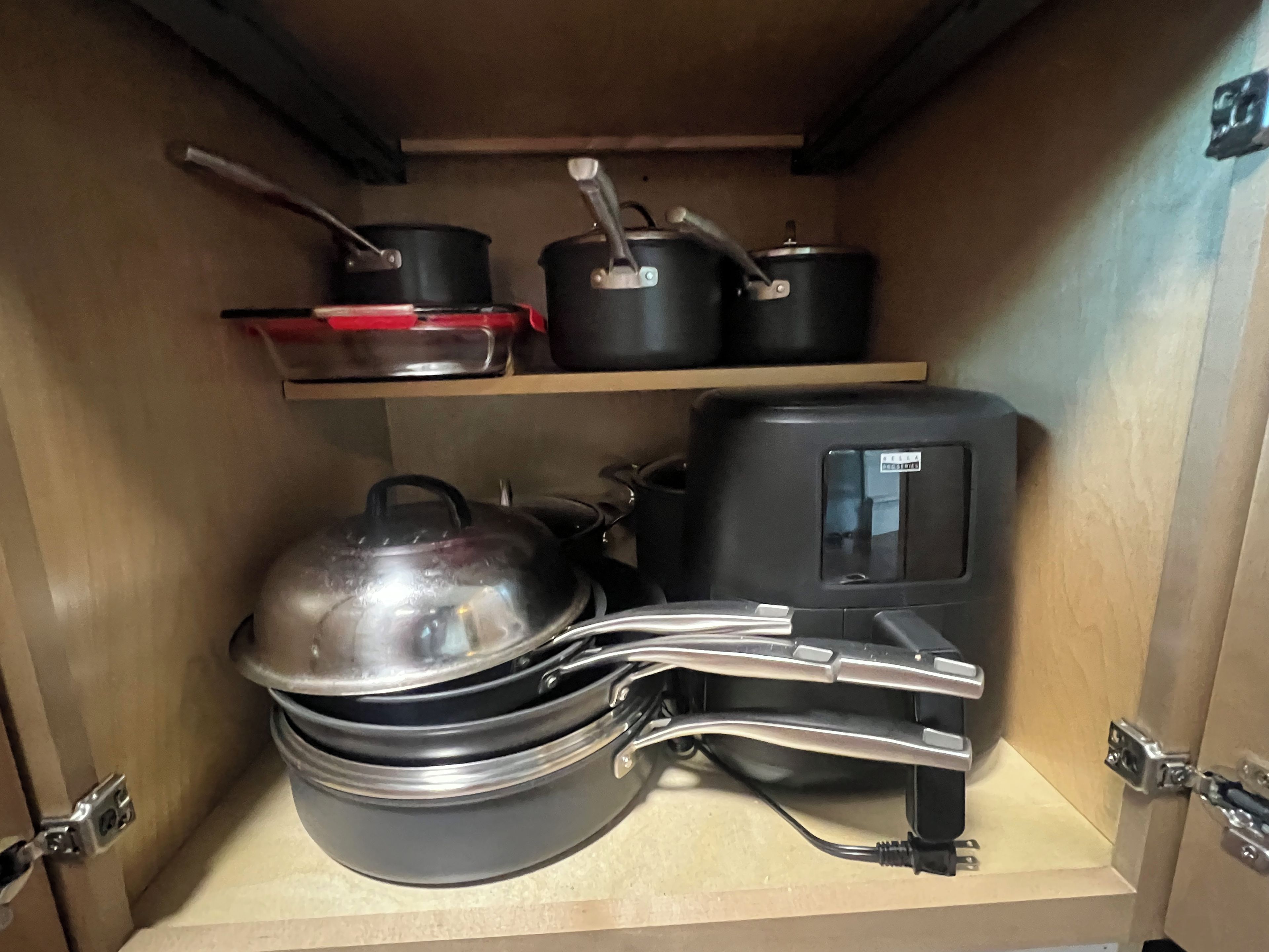 Un armario de cocina con estantes que contienen ollas, sartenes y una tetera.