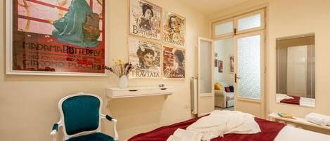 Une chambre d’hôtel avec un lit, une chaise bleue, un bureau blanc et une grande affiche accrochée au mur.