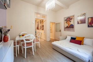 A modern bedroom with a white bed, colorful pillows, a dining area with white chairs, and a chandelier. - Two Minutes from Florence Cathedral   San Lorenzo Terrace (FIRENZE)