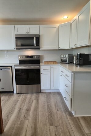A kitchen with white cabinets, a microwave, an oven, a toaster, and a coffee maker. - Cozy, family-friendly, 3-bedroom canal-front house in Nokomis 7-min to the beach (Nokomis)