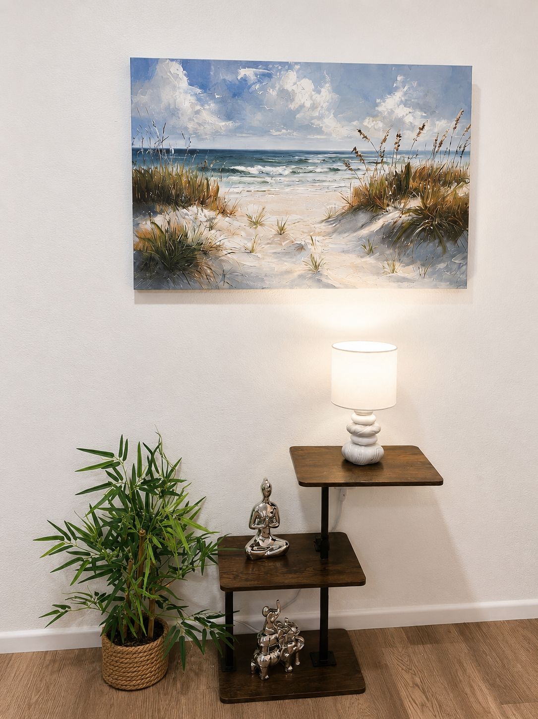 A painting of a beach scene on a wall, a lamp on a small table, and a bamboo plant.
