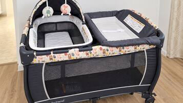 A portable baby travel crib with a mesh bottom and a cushioned top, featuring a bear and fox design.
