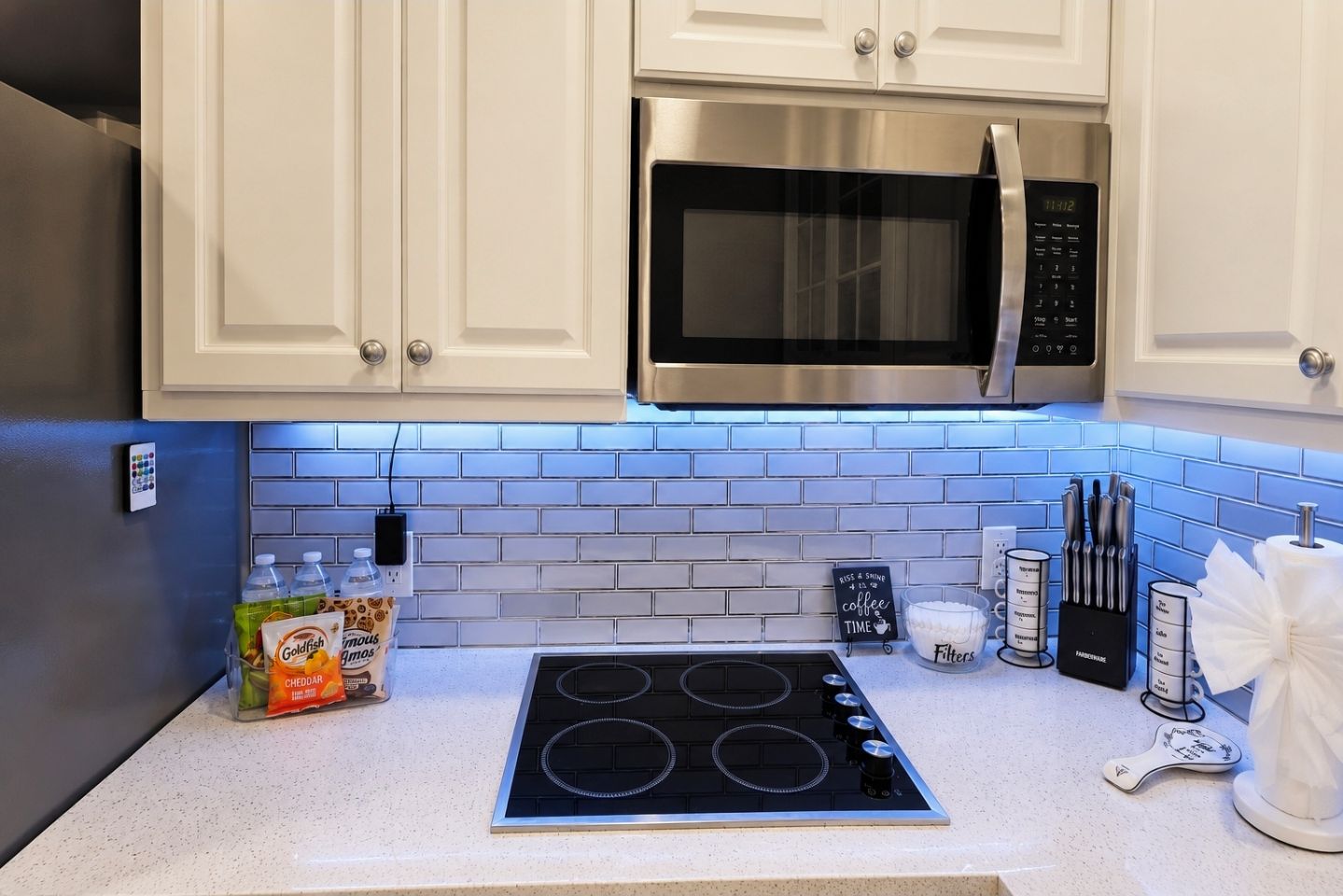 A kitchen with white cabinets, a stainless steel microwave, a black stove, and a blue-tiled backsplash.