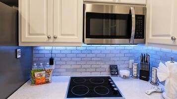 A kitchen with white cabinets, a stainless steel microwave, a black stove, and a blue-tiled backsplash.