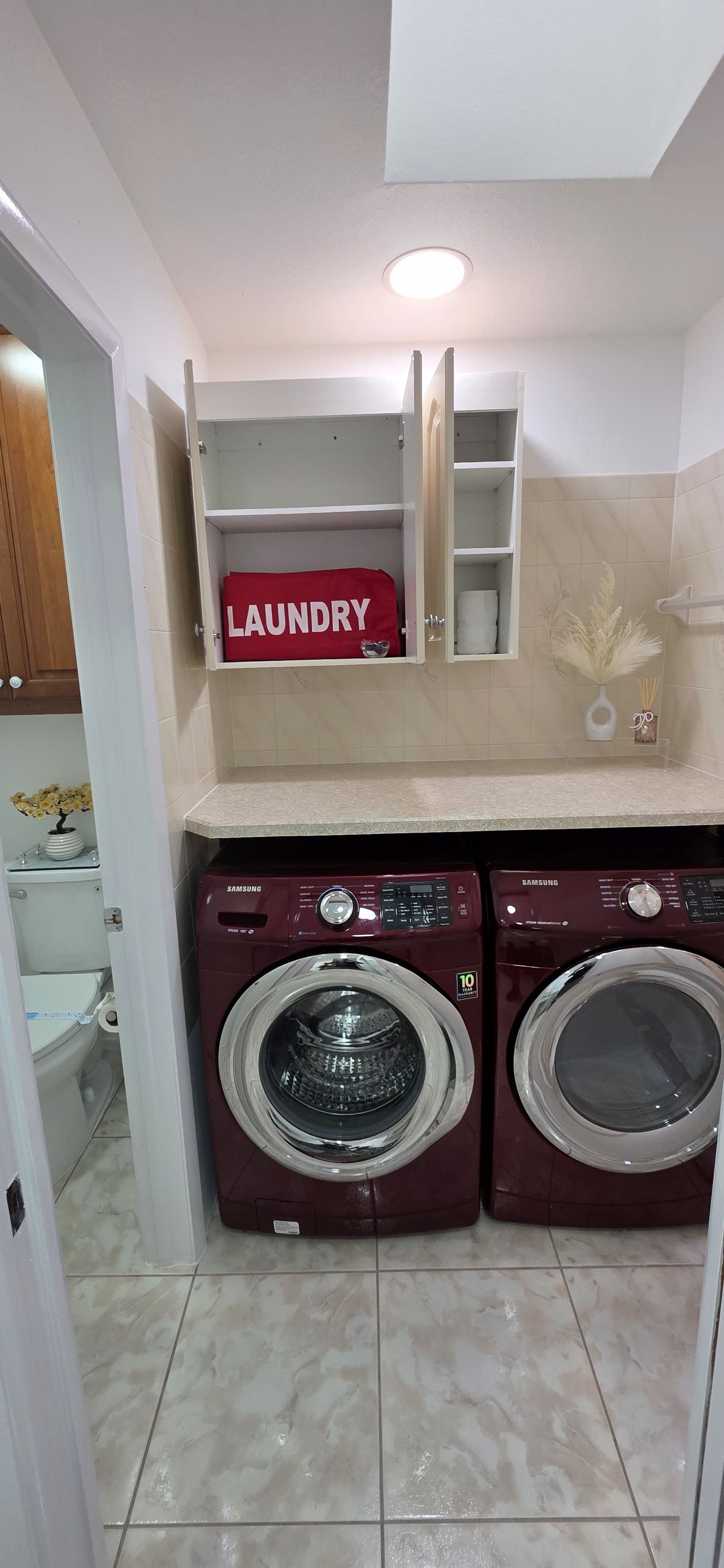 A laundry room with two washing machines, a shelf with a 'laundry' sign, and a toilet visible in the background.