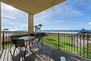 Ein Balkon mit Tisch und Stühlen, der Blick auf einen Strand mit Palmen und einem klaren Himmel gewährt.