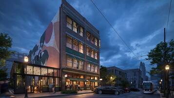 A multi-story hotel with a prominent mural on the side, a ground-level restaurant, and a tram line in the background.