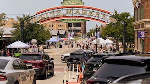 Una calle concurrida con un arco histórico que indica 'Kansas City' y '1857', año de fundación de la ciudad.