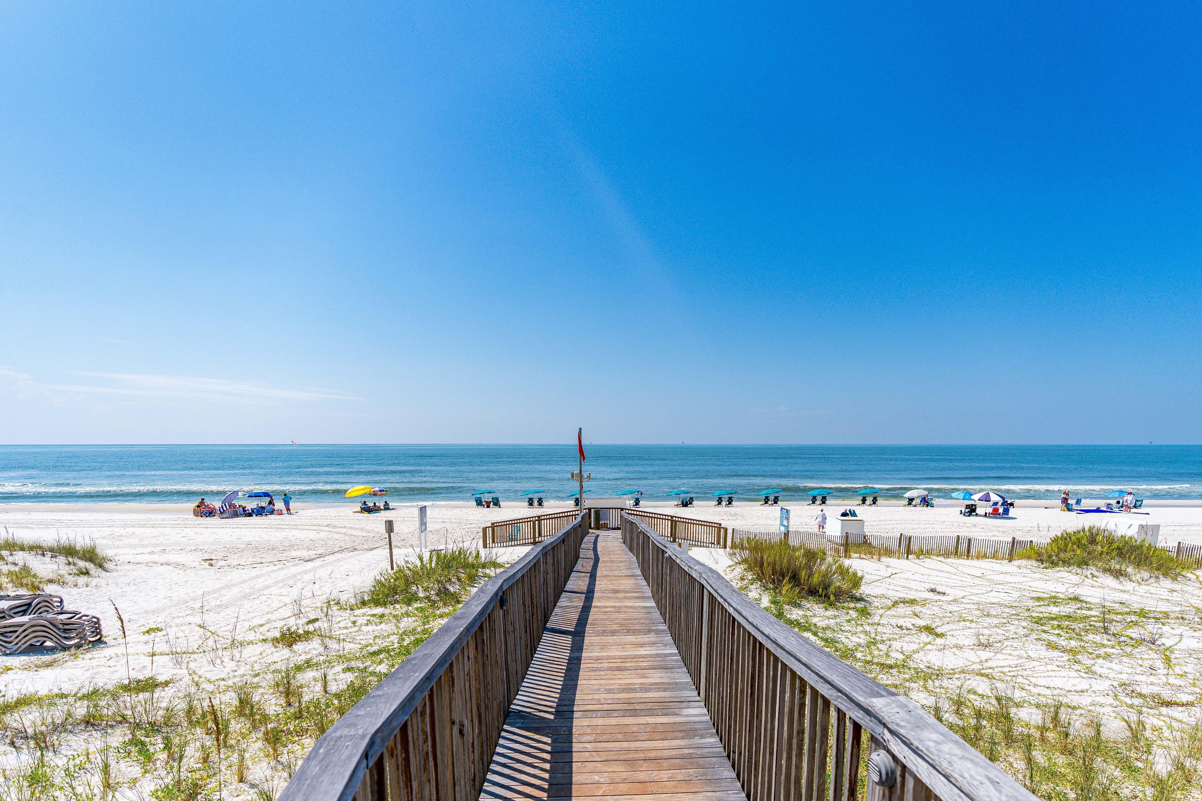 A wooden boardwalk leading to a beach with umbrellas and beach chairs.