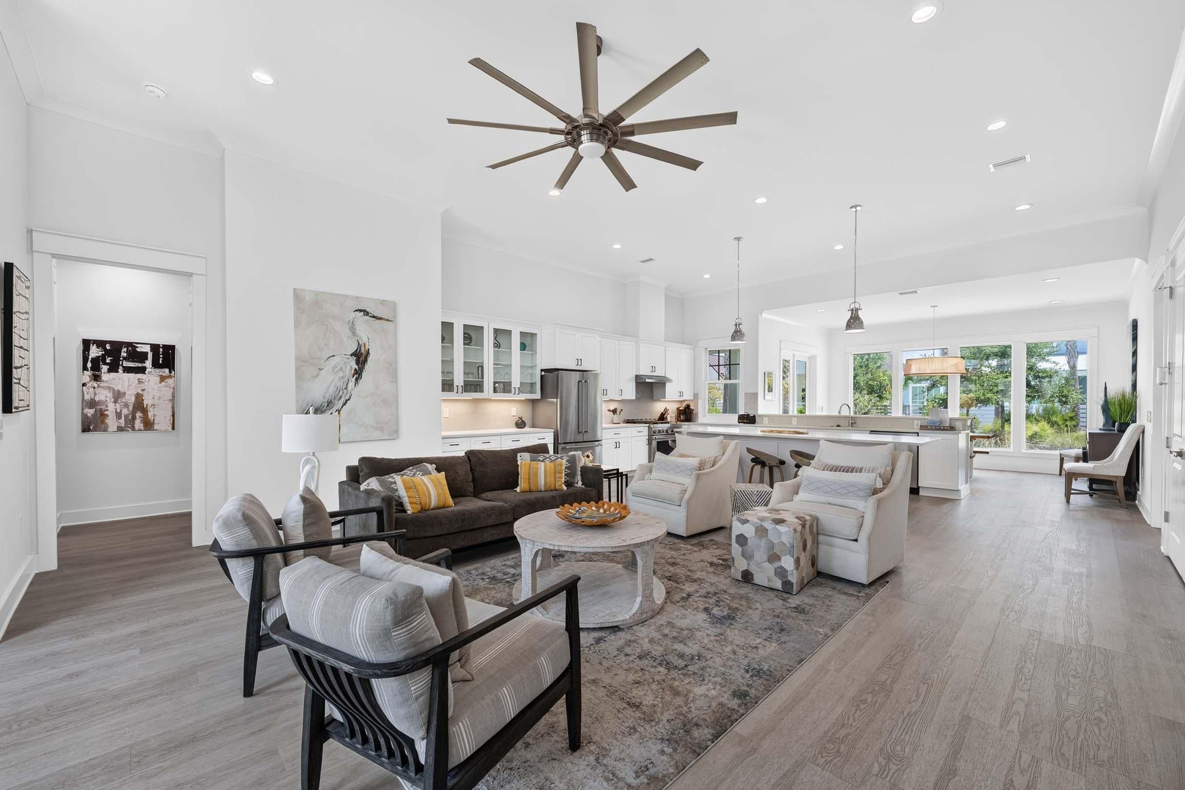 A spacious living room with a large ceiling fan, a kitchen with white cabinets, and a dining area with a round table.