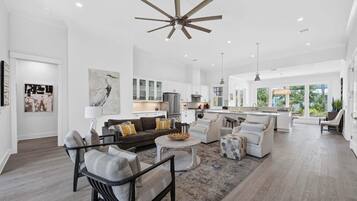 A spacious living room with a large ceiling fan, a kitchen with white cabinets, and a dining area with a round table.