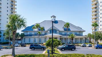 A multi-story hotel with a central entrance, parking lot, and surrounding palm trees.