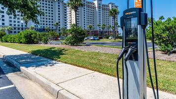 A chargepoint+ electric vehicle charging station on a sidewalk with a road and buildings in the background.
