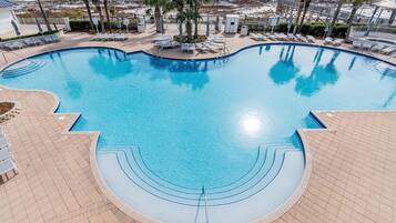 A swimming pool with a curved design, surrounded by lounge chairs and palm trees, with a beach and ocean view in the background.