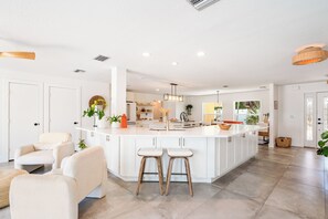 Une cuisine spacieuse dotée d’un grand îlot central, de meubles blancs et d’un éclairage moderne suspendu au plafond.